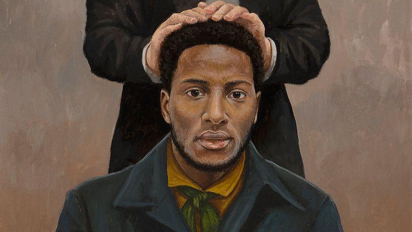 A white man in a black suit places his hands on the head of a black man, Q. Walker Lewis.