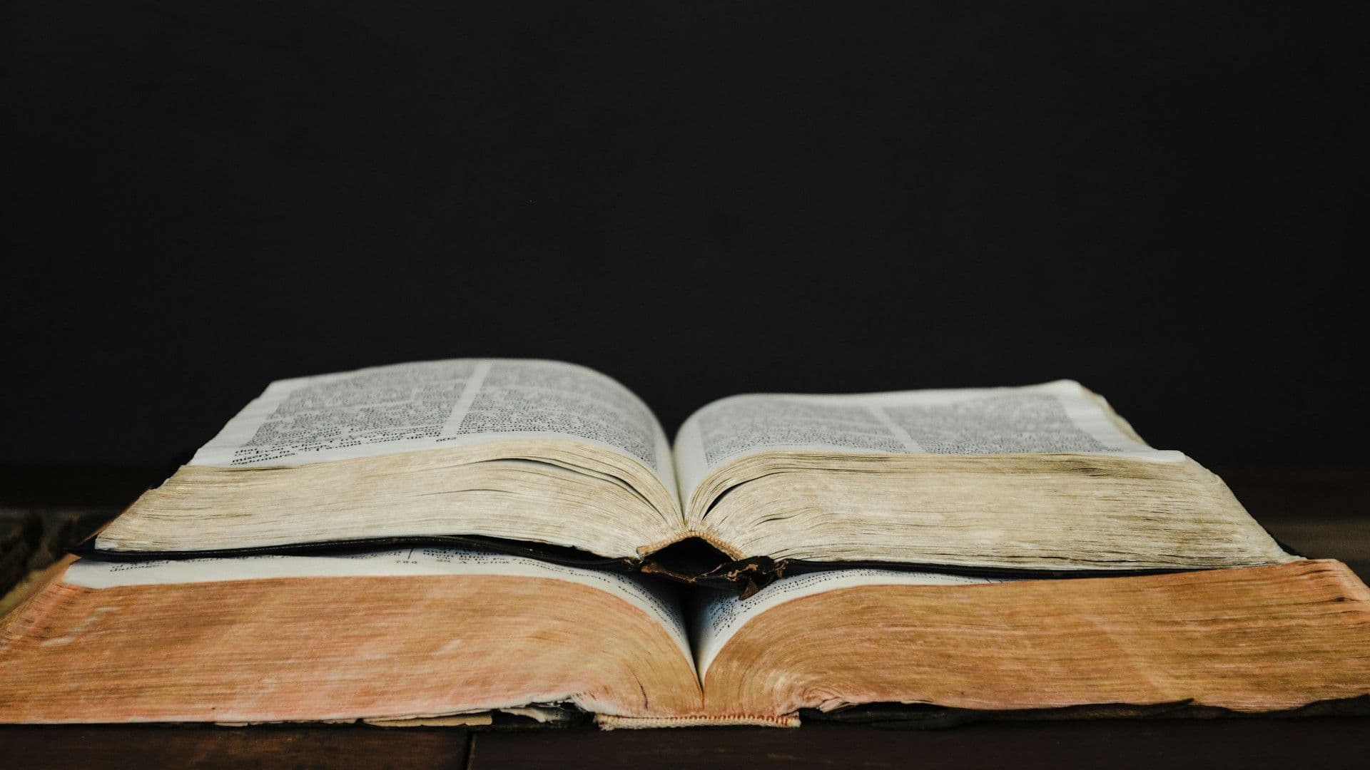 Two open books, one stacked on top of the other, in front of a black background